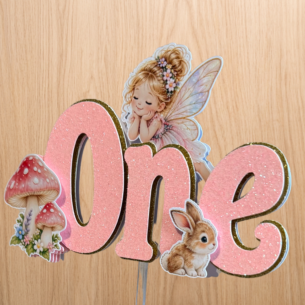 Handmade layered fairy garden first birthday cake topper showing dimensional glitter lettering